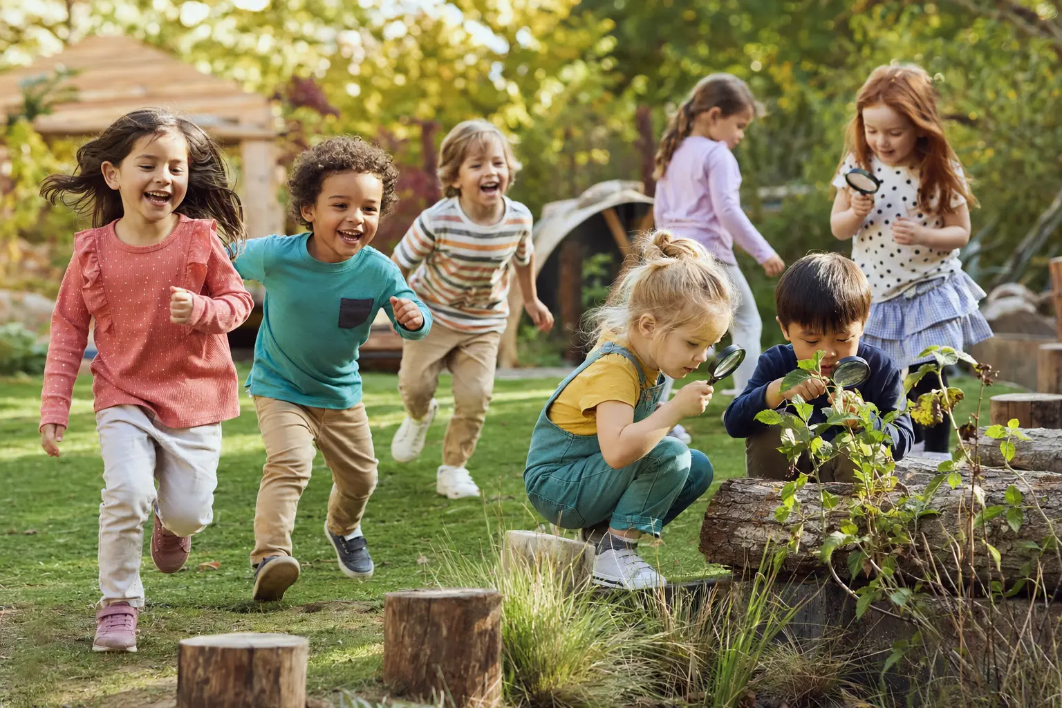 Children running and exploring plants with magnifying glasses in a natural play garden