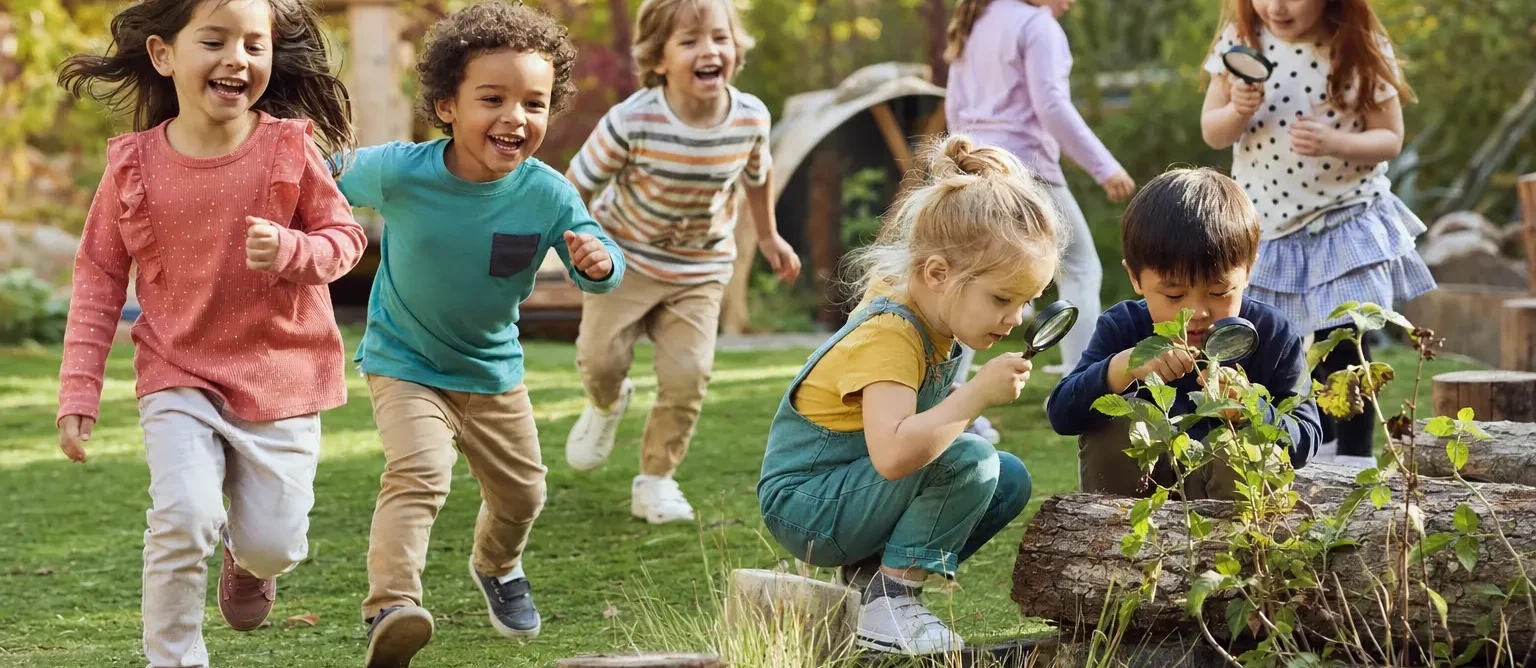 Children running and exploring plants with magnifying glasses in a natural play garden